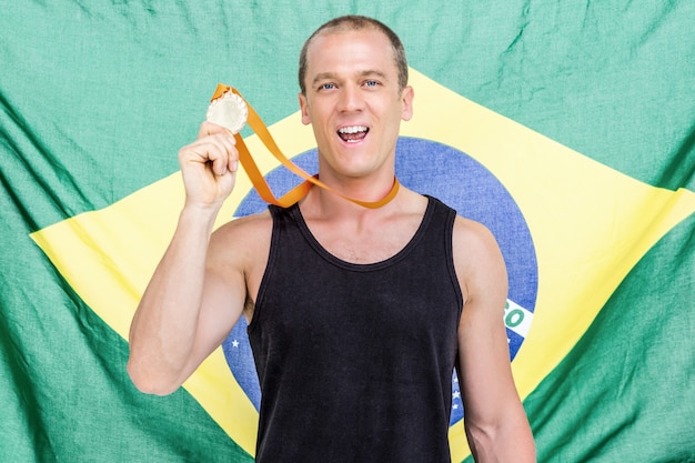 Atleta mostrando sua medalha de ouro na frente da bandeira do Brasil