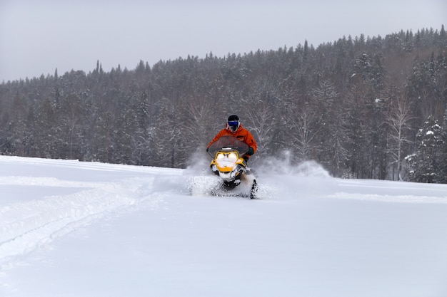 Atleta en una moto de nieve en el bosque de invierno.