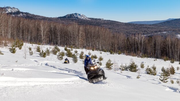 Atleta en una moto de nieve en el bosque de invierno.