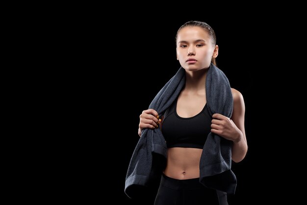 Foto atleta muito jovem em forma, segurando uma toalha cinza macia no pescoço enquanto está isolada