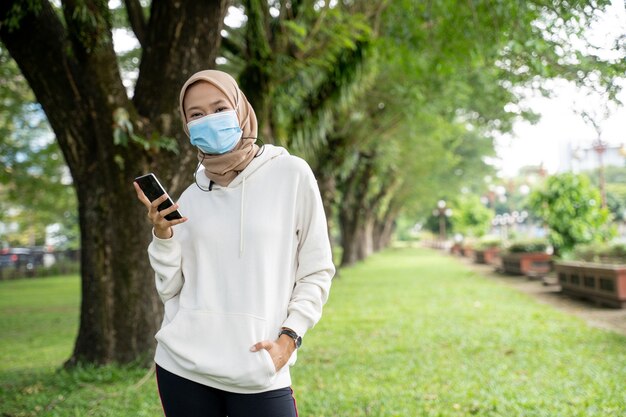 Atleta mujer bastante musulmana con mascarilla mirando a cámara mientras hace ejercicio al aire libre