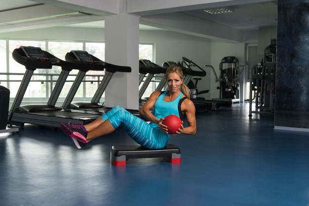 Atleta de mujer madura haciendo ejercicio de abdominales con bola en paso a paso como parte del entrenamiento de culturismo