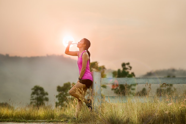 Atleta mulheres bebendo água depois de correr no pôr do sol do céu