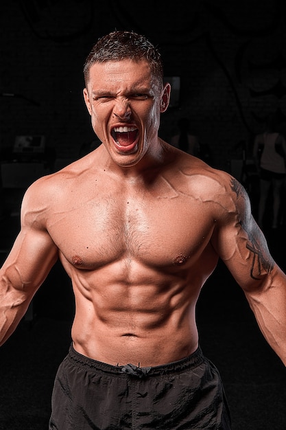 Atleta muscular culturista brutal emocional posando en el gimnasio. el fondo es negro