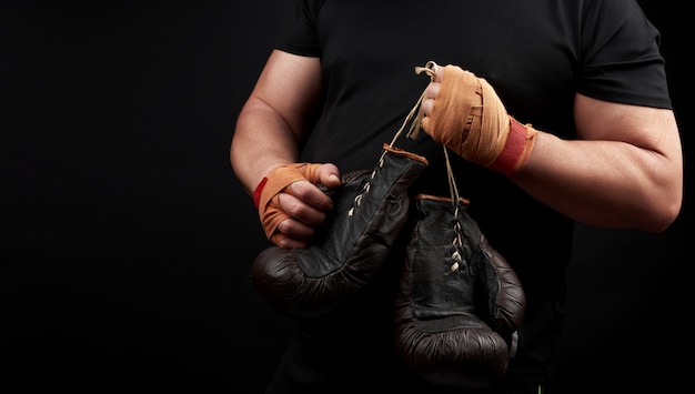 Atleta muscular em um uniforme preto tem luvas de boxe marrons muito antigas na mão