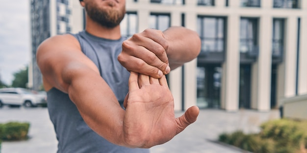 Foto atleta musculoso con barba estira los brazos antes de entrenar mientras está de pie en la calle