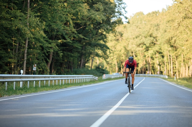 Atleta musculoso en casco negro, gafas y ropa activa montando bicicleta con alta velocidad en la carretera asfaltada