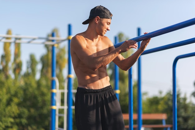 Atleta musculoso jovem macho malhando no campo esportivo ao ar livre desportista bonito praticando estilo de vida saudável modelo masculino sem camisa exercitando no bar do lado de fora pessoas e conceito de esporte