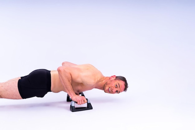 Atleta musculoso sem camisa fazendo push-up em barras de push-up homem de corpo inteiro em fundo branco de estúdio