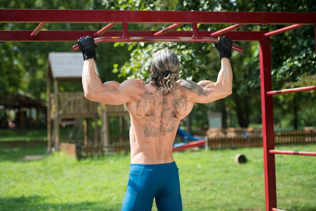 Atleta musculoso trabajando en un gimnasio al aire libre haciendo dominadas