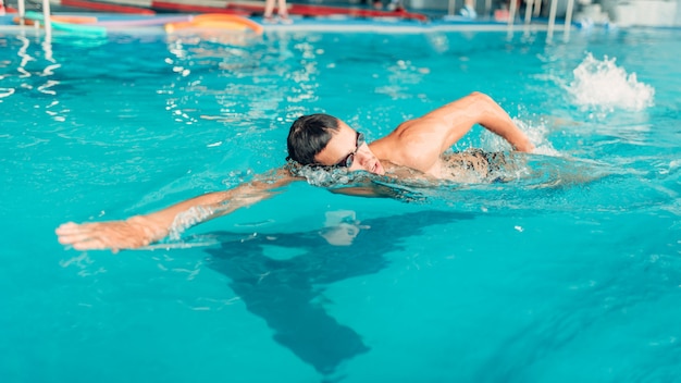 Atleta nadador de óculos nada na piscina coberta.