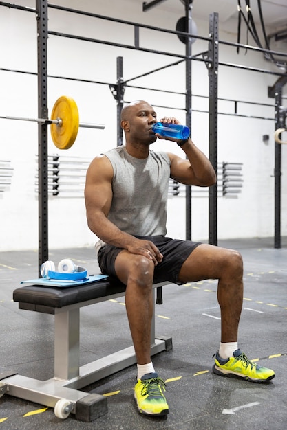 Atleta negro bebendo água após treino no ginásio. Esporte e estilo de vida saudável.