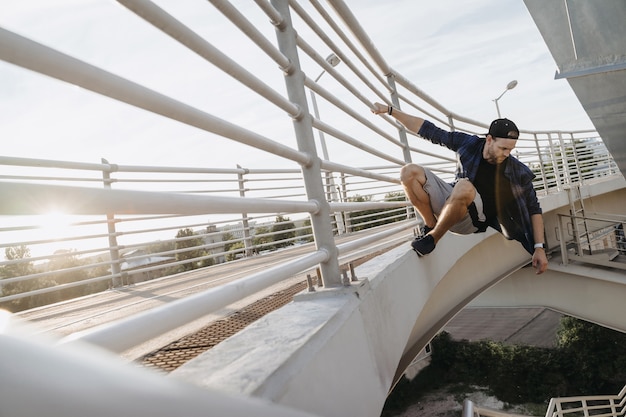 Atleta de parkour colgado del puente y listo para un salto peligroso. Freerunning en la ciudad