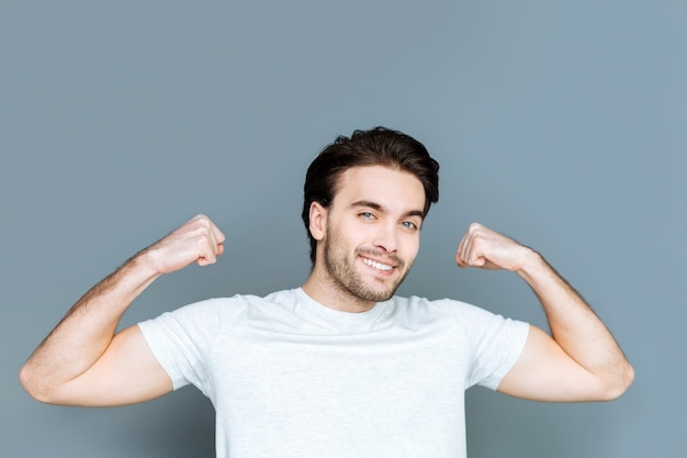 Atleta profesional. Alegre hombre brutal bien construido sonriendo y mostrando su cuerpo mientras disfruta de actividades deportivas