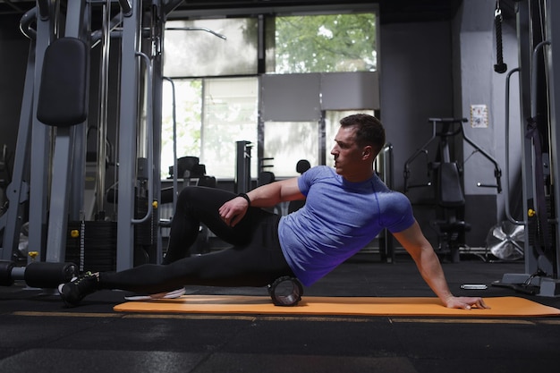 Atleta profesional estirando los músculos usando un rodillo de espuma en el gimnasio
