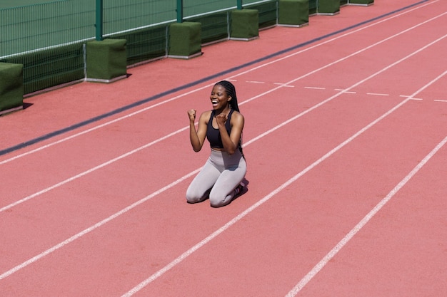 Atleta profissional negra em roupas esportivas se alegra com sucesso na corrida de longa distância na pista