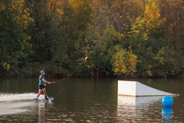 Un atleta realiza un truco en el parque acuático al atardecer. Jinete de Wakeboard