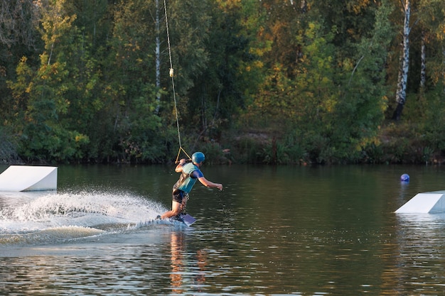 Un atleta realiza un truco en el parque acuático al atardecer. Jinete de Wakeboard