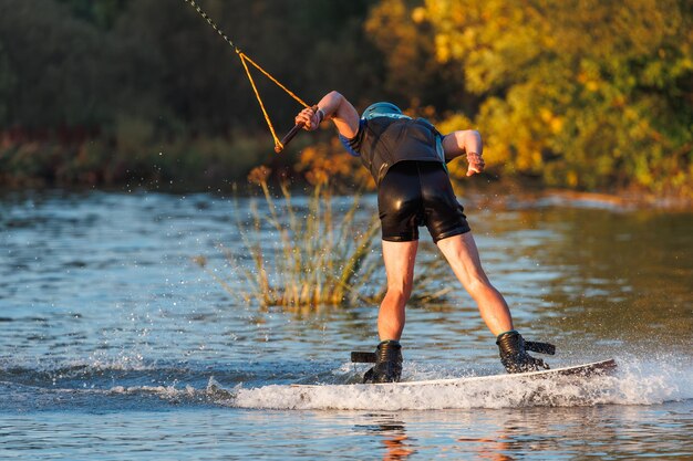 Un atleta realiza un truco en el parque acuático al atardecer. Jinete de Wakeboard