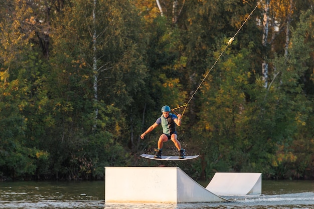 Un atleta salta sobre el agua Parque de Wakeboard al atardecer Un ciclista realiza un truco en la tabla