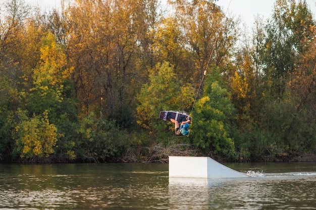 Un atleta salta desde un trampolín en el parque de Wakeboard al atardecer. Un hombre realiza un truco en una tabla.