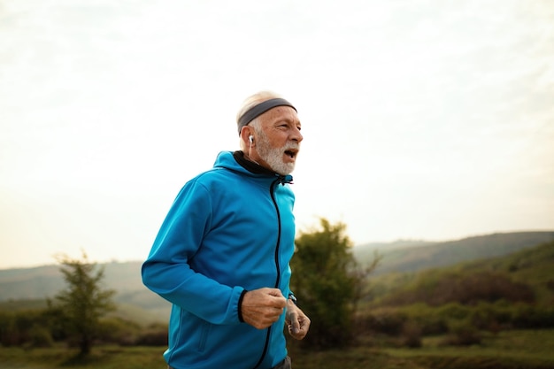 Atleta senior activo trotando por la mañana y escuchando música en auriculares en la naturaleza Copiar espacio