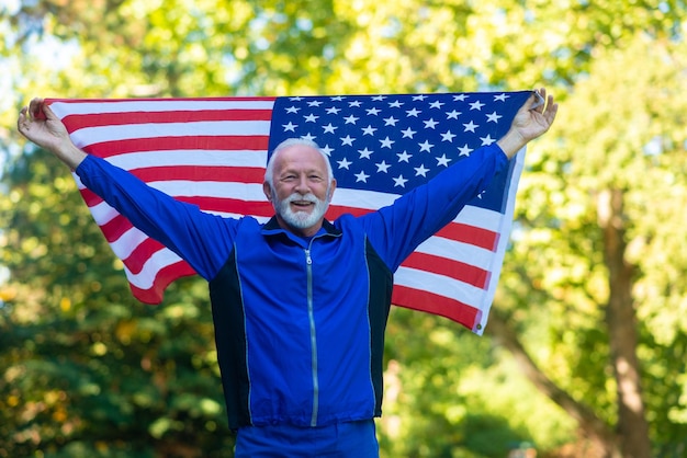 El atleta senior sostiene la bandera estadounidense en el parque.