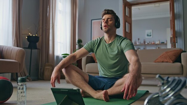 Atleta sereno meditando con auriculares en el apartamento hombre en forma tranquilo sentado en el loto