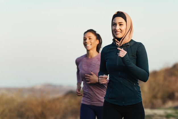 Atleta sonriente y su entrenador personal trotando por la mañana en la naturaleza