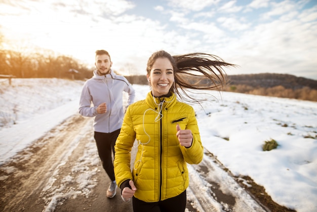 Atletas activos pareja deportiva corriendo con gran persistencia en el camino en la naturaleza de invierno en la mañana.