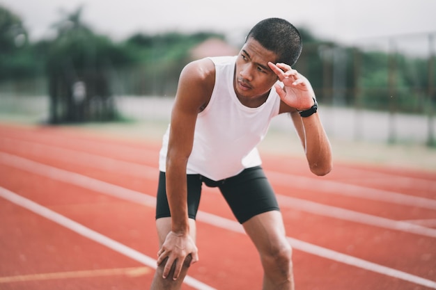 Atletas esporte homem corredor vestindo roupas esportivas brancas cansadas de limpar o suor e descansar depois de praticar em uma pista de corrida em um estádio Conceito de esporte de corredor