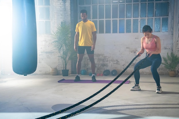 Atletas de fitness entrenando usando cuerdas de batalla ejercicio intenso en el gimnasio amigos disfrutando