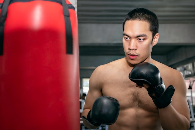 Atletas hombre asiático boxeador entrenando en un saco de boxeo en el gimnasio