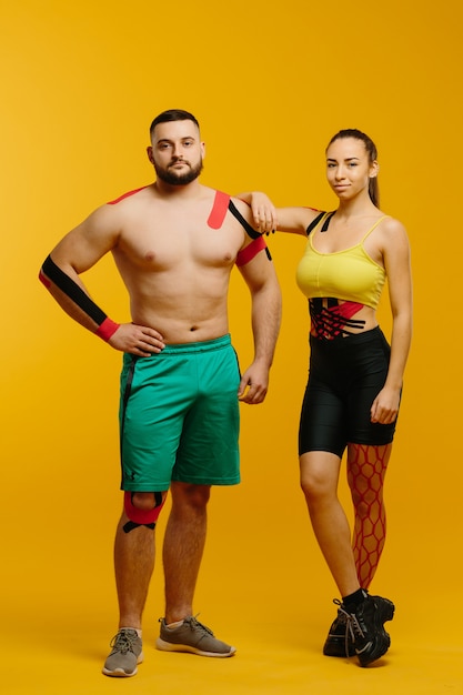 Atletas profesionales, hombre y mujer con cinta kinesiológica en el cuerpo, posando en amarillo