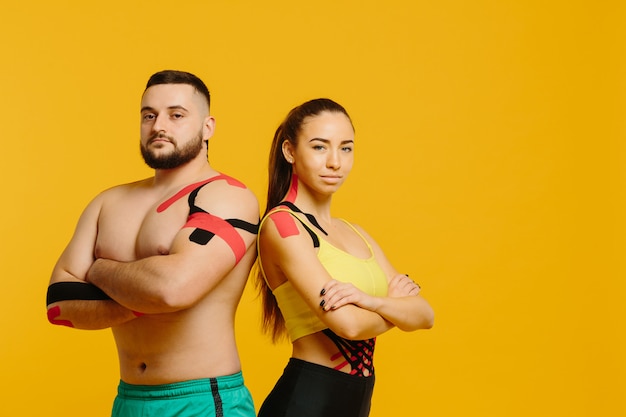 Atletas profesionales, hombre y mujer con cinta kinesiológica en el cuerpo, posando en amarillo