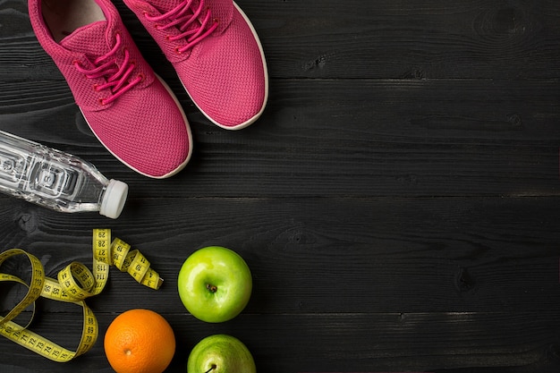 Los atletas con zapatillas de deporte de ropa femenina y una botella de agua sobre fondo oscuro