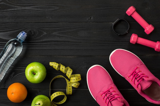 Los atletas con zapatillas de deporte de ropa femenina y una botella de agua sobre fondo oscuro