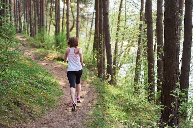 Atlética jovem de tênis rosa correr na floresta de primavera