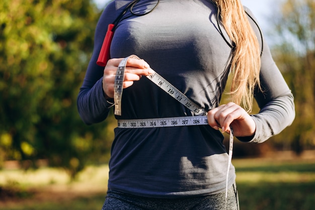 Foto atlética mulher magro, medindo a cintura por fita métrica após treino ao ar livre