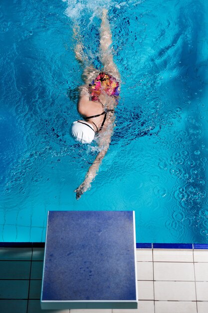 Atlética mulher nadando com boné e óculos na piscina