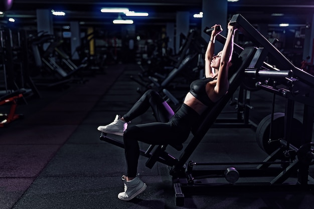 Atlética mulher sexy fazendo exercício usando a máquina no ginásio - vista lateral