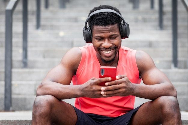 Atlético afro-americano ouve música em fones de ouvido sem fio e sorri ao ar livre