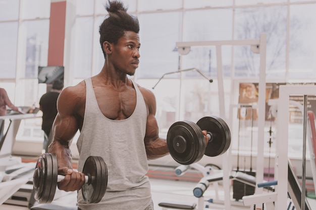 Atlético homem Africano malhando com halteres na Academia