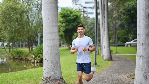 Atlético homem asiático bonito correndo no parque verde praticando para sua maratona