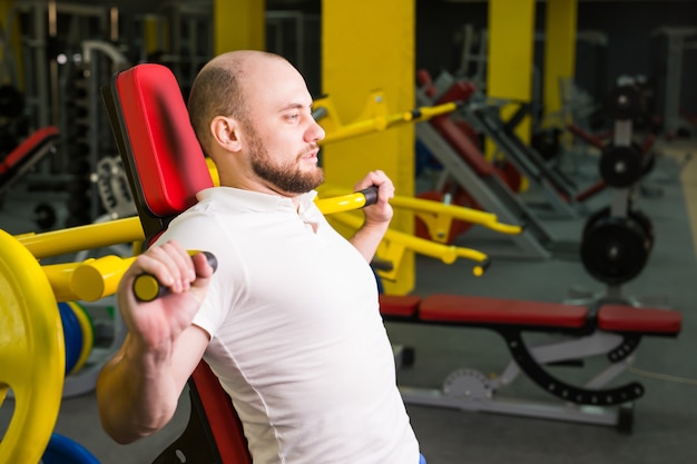 Atlético homem fazendo exercícios com máquina de exercício de força em um clube de ginástica