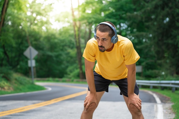 Atlético jovem se sentindo cansado e descansando enquanto recupera o fôlego depois de correr em um caminho.