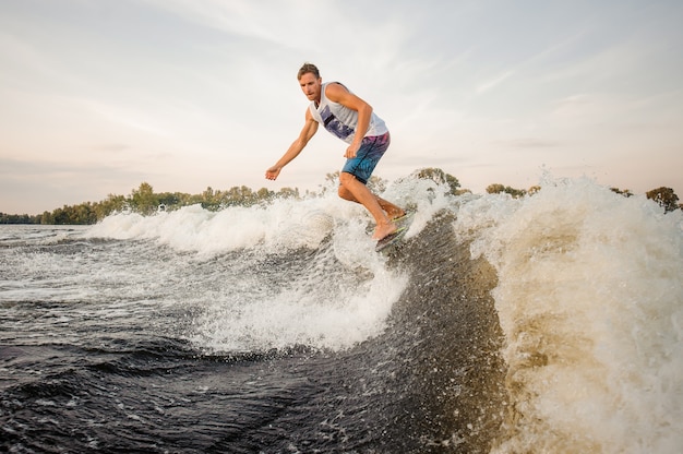 Foto atlético wakesurfer pulando a bordo, descendo as ondas do rio