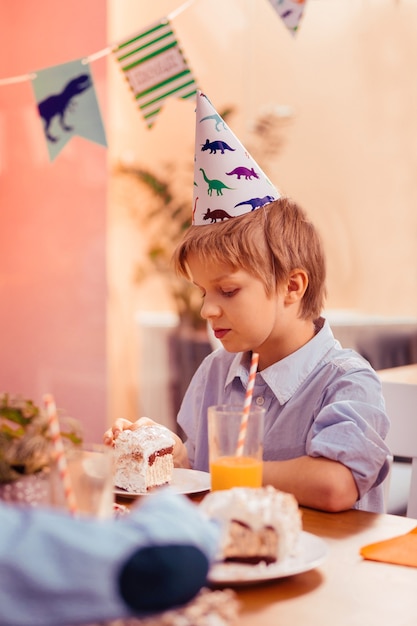 Atmósfera aburrida. Muchacho concentrado inclinando la cabeza mientras mira el postre en la placa