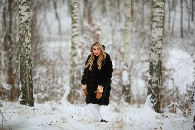 Atmosfera de inverno na floresta Retrato de uma loira com um casaco de pele preto