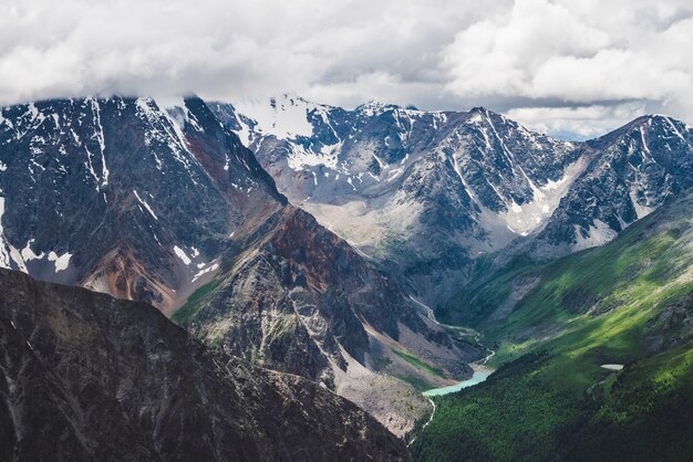 Atmosférico paisaje alpino con enorme glaciar colgante en rocas gigantes y valle con lagos de montaña. Gran lengua glaciar. Nubes bajas sobre montañas nevadas. Majestuoso paisaje a gran altitud.